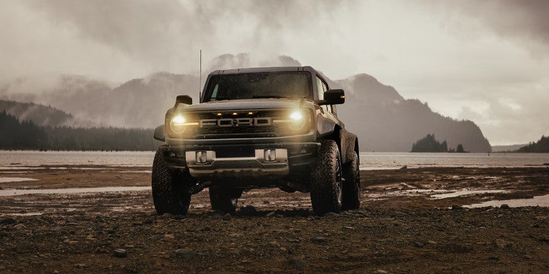 Ford off-road SUV with headlights on, parked by a lake with mountains in background