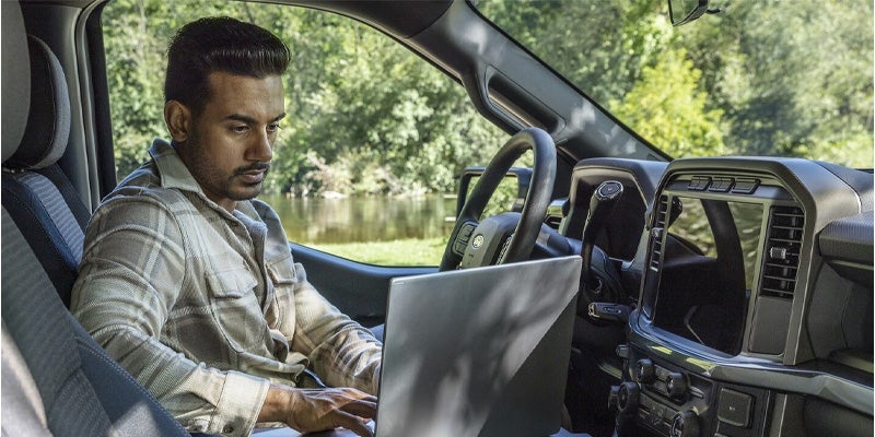 A man is sitting inside Ford F-150 with a laptop.